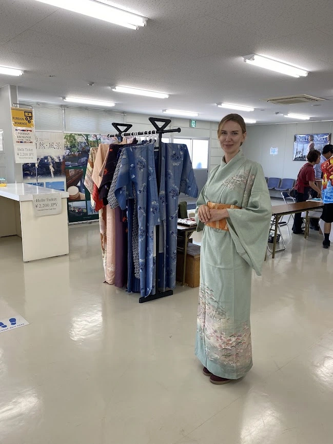 Person wearing a pale green Japanese kimono beside a rack of kimono in Japan
